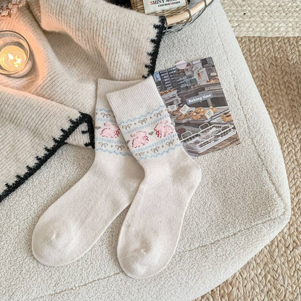 Pair of white socks with floral lace trim on a textured surface with a candle and magazine in the background.