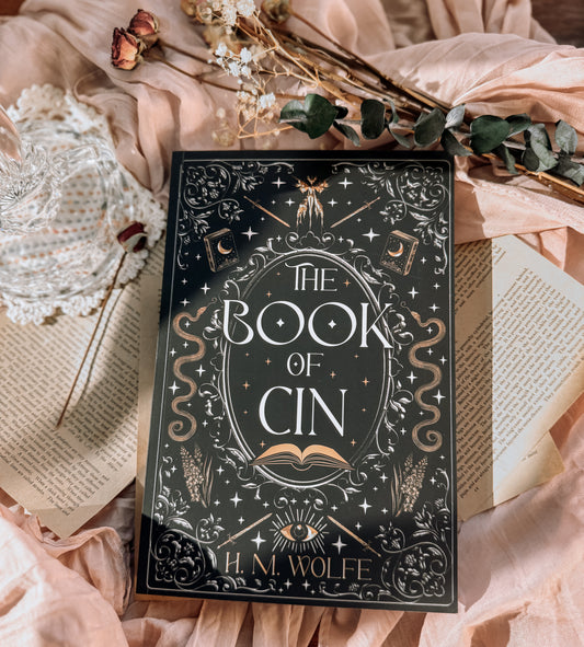 Book titled 'The Book of Cin' by H.M. Wolfe on a decorative surface with flowers and lace.