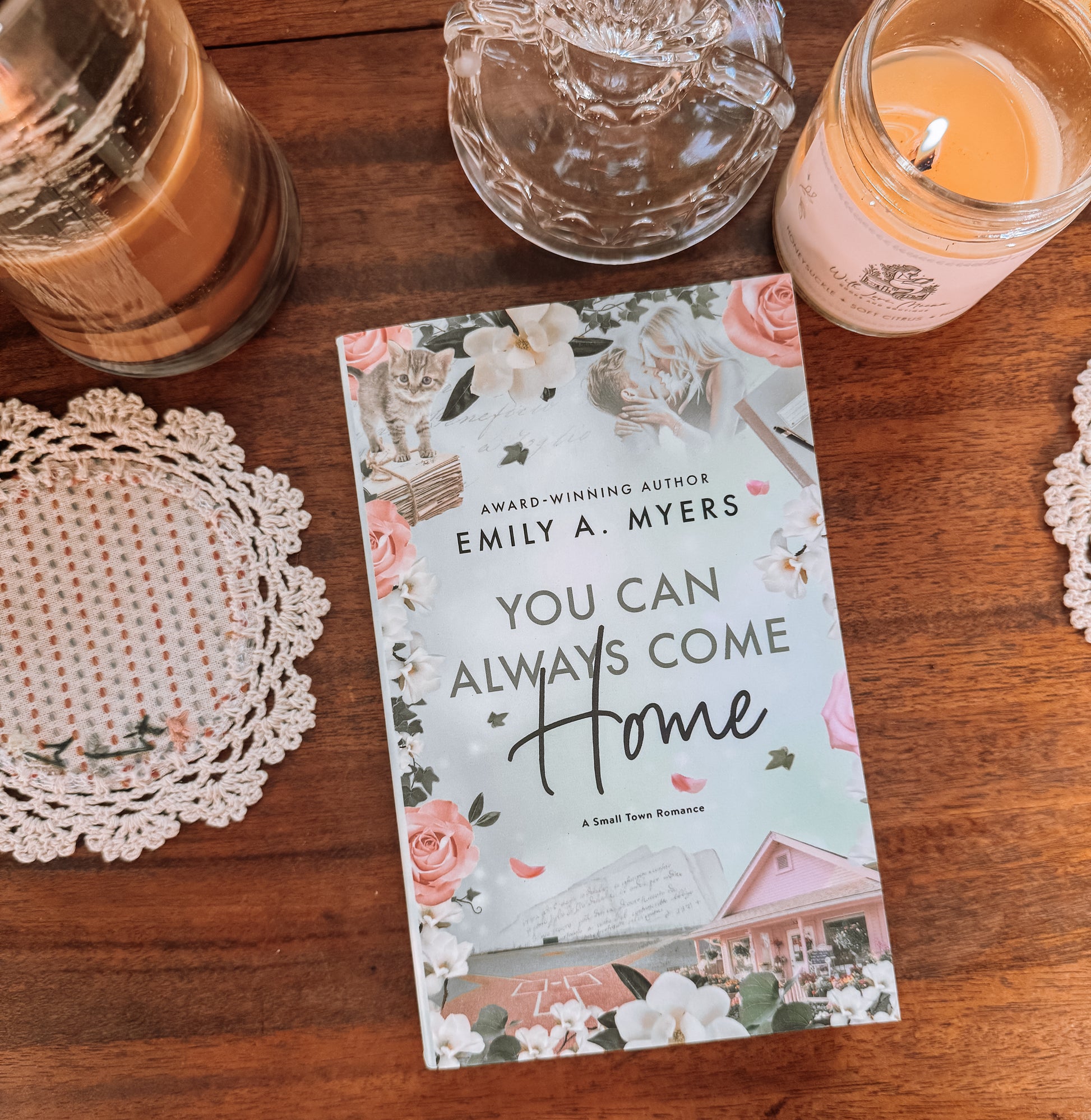 Book titled 'You Can Always Come Home' by Emily A. Myers on a wooden surface with candles and doilies.