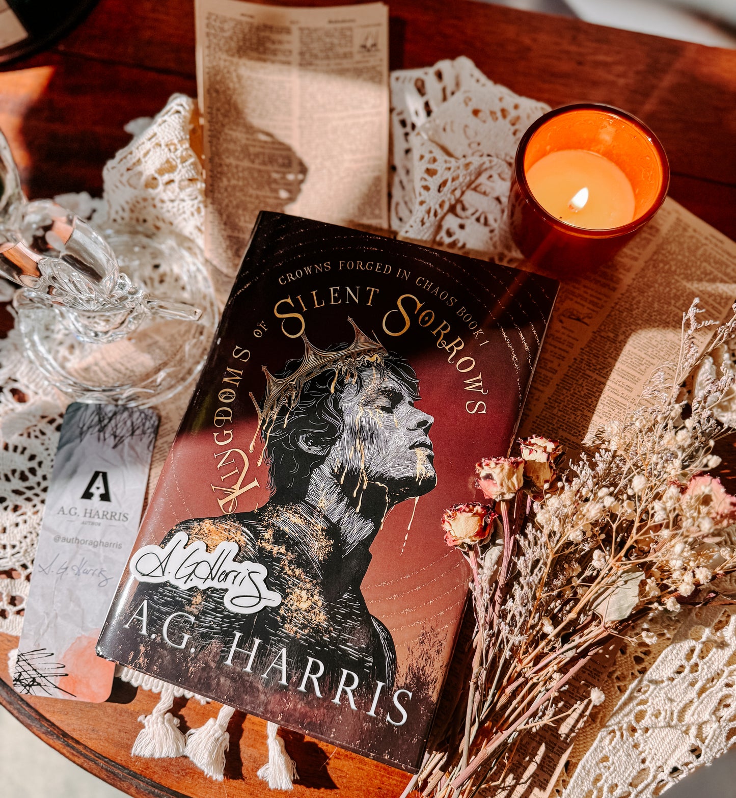 Book titled 'Silent Sorrows' by A.G. Harris on a wooden surface with a candle and decorative items.