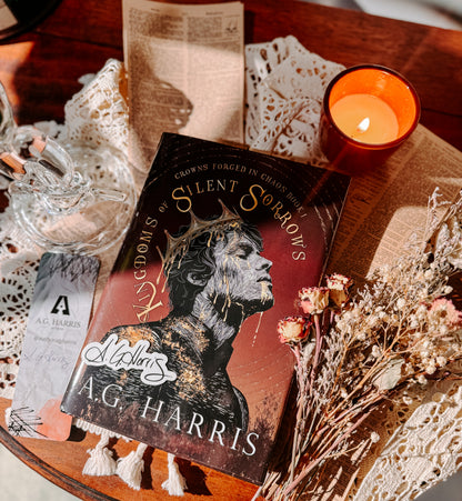 Book titled 'Silent Sorrows' by A.G. Harris on a wooden surface with a candle and decorative items.