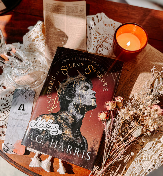 Book titled 'Silent Sorrows' by A.G. Harris on a wooden surface with a candle and decorative items.