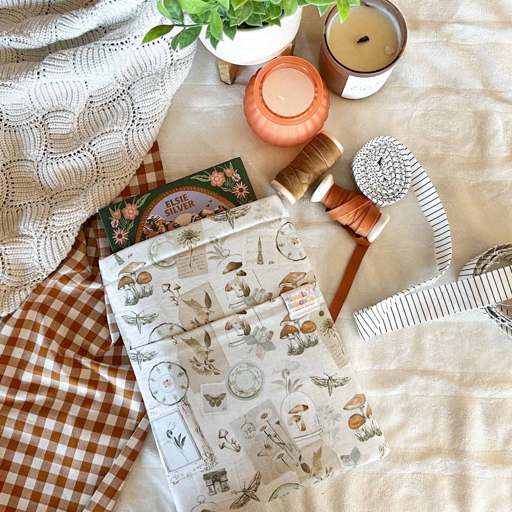 Flat lay of stationery items including a notebook, candles, and a plant on a textured surface. Book sleeve 