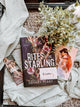 Book titled 'Rites of the Starling' by Devney Perry on a textured surface with a plant and other books.