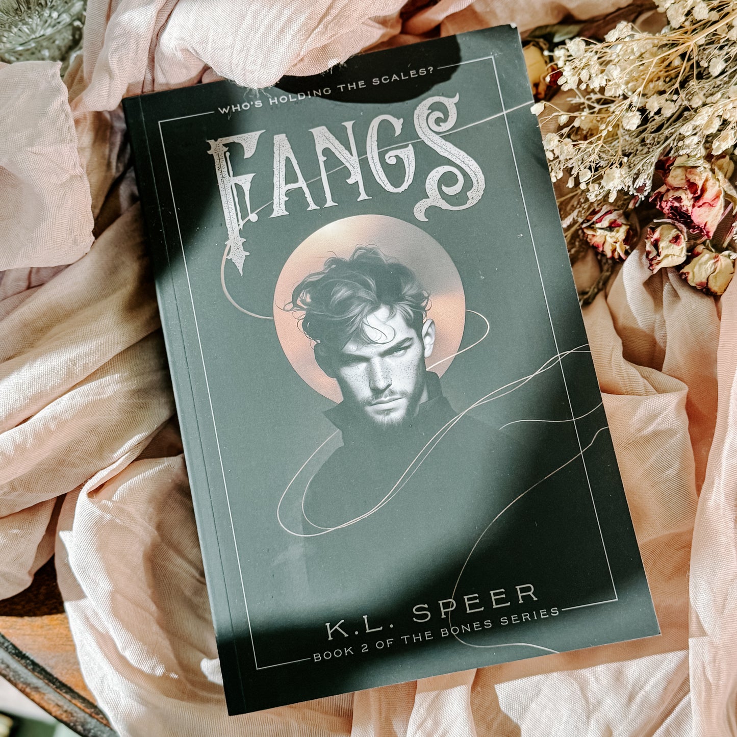 Book titled 'Fangs' by K.L. Speer on a soft fabric background with flowers.