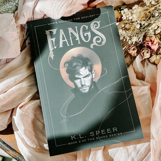 Book titled 'Fangs' by K.L. Speer on a soft fabric background with flowers.