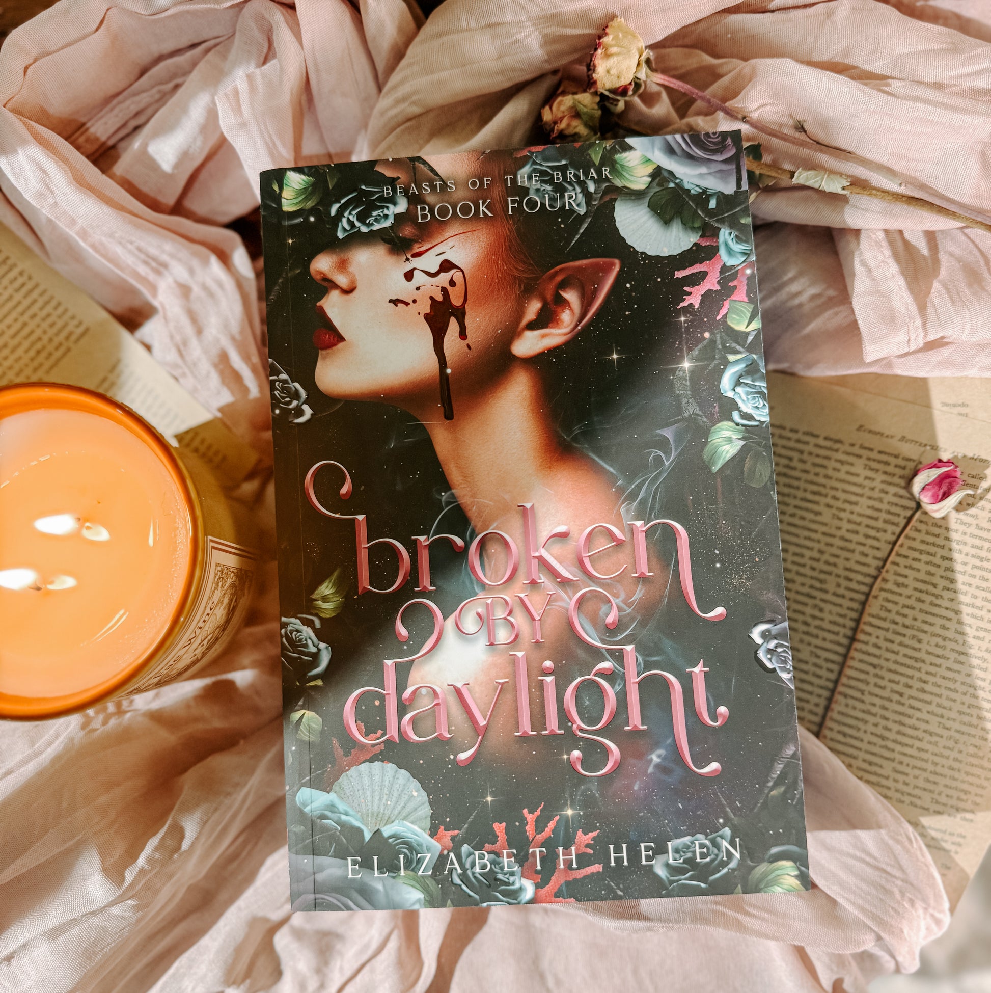 Book titled 'Broken by Daylight' by Elizabeth Helen on a soft fabric background with a candle.