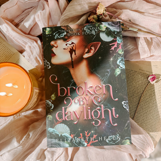 Book titled 'Broken by Daylight' by Elizabeth Helen on a soft fabric background with a candle.