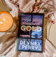 Book titled 'Bluebird Gold' by Devney Perry with a candle and flowers on a soft fabric background