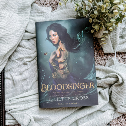 Book titled 'Bloodsinger' by Juliette Cross on a textured surface with plants.