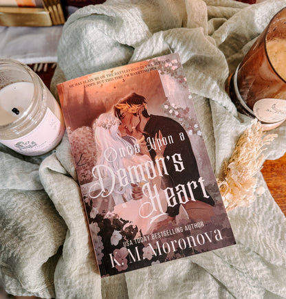 Book titled 'once upon a Demon's Heart' by K.M. Moronova on a textured surface with candles and decor.