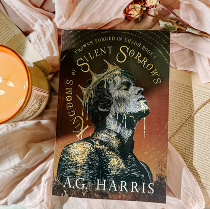 Book titled 'kingdom  of Silent Sorrows' by A.G. Harris on a soft fabric background with flowers and a candle.
