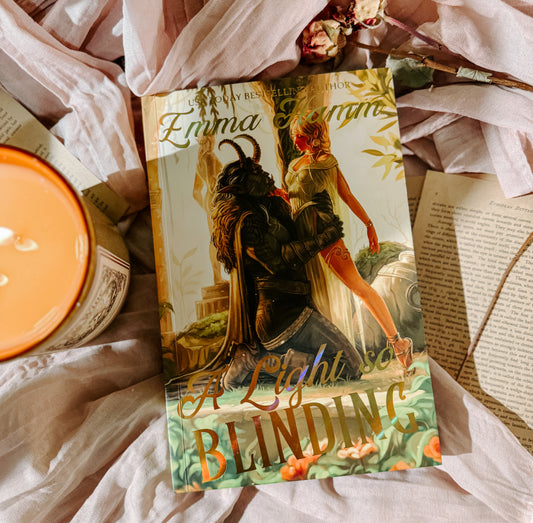 Book titled 'A Light Blinding' by Emma Newman on a soft fabric background with a candle.