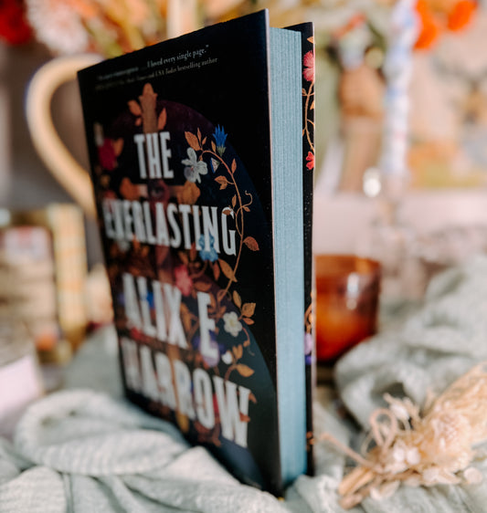 Book titled 'The Everlasting' by Alix E. Harrow on a soft surface with a candle in the background