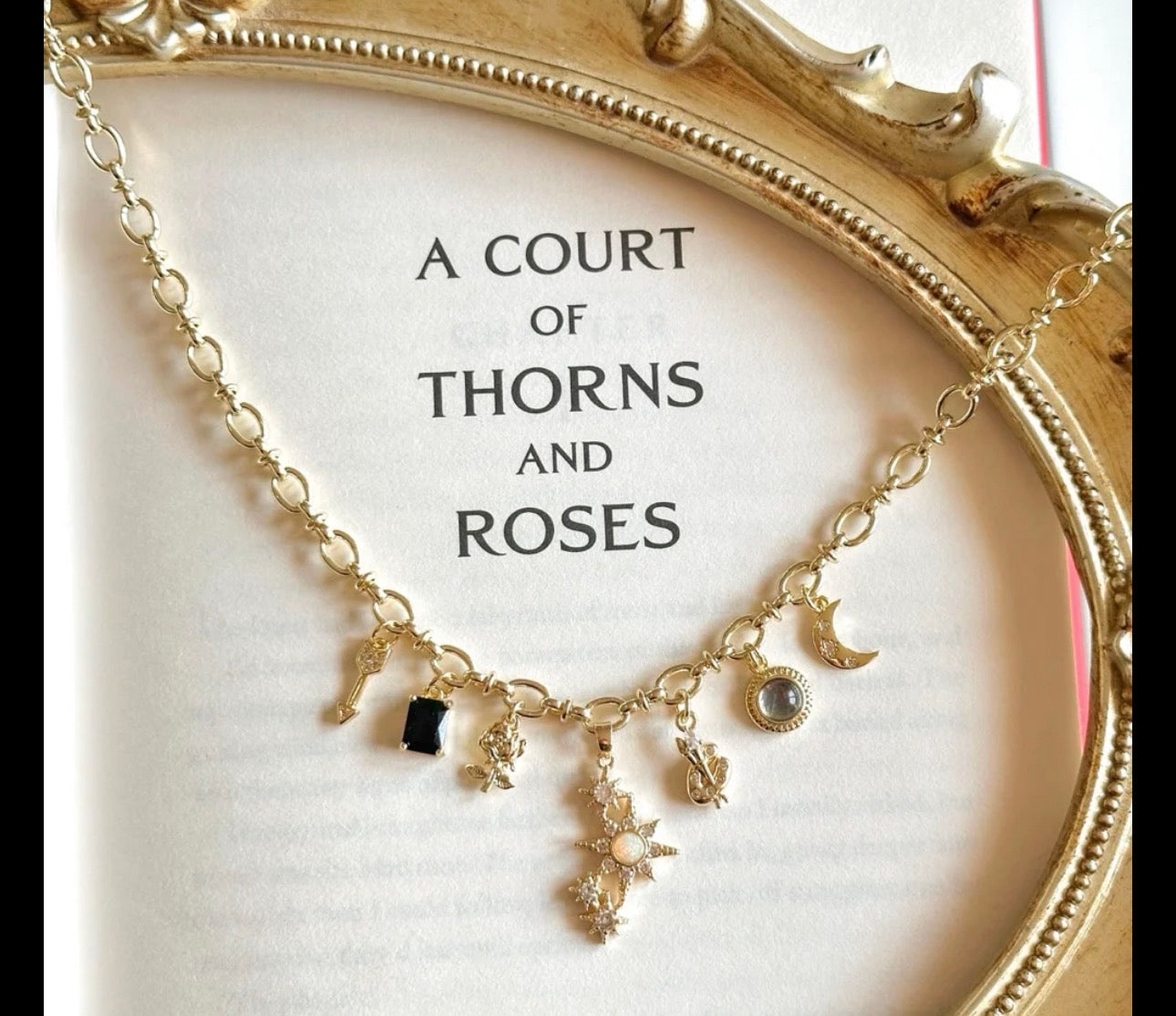 Gold necklace with charms on a card titled 'A Court of Thorns and Roses'.