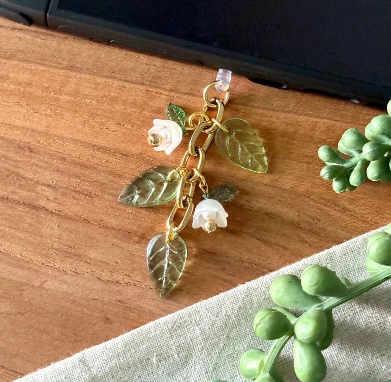 Gold charm with leaves and flowers on a wooden surface dust plug Charm 