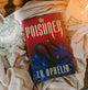 Book titled 'The Poisoner' by L.N. Ophelia on a textured surface with a candle in the background.