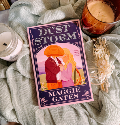 Book titled 'Dust Storm' by Maggie Gates on a textured surface with a candle and decorative elements.