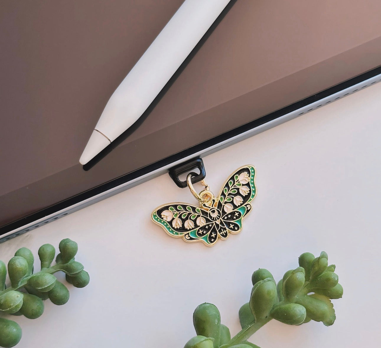 Butterfly-shaped phone charm on a laptop with green plants in the foreground dust plug 