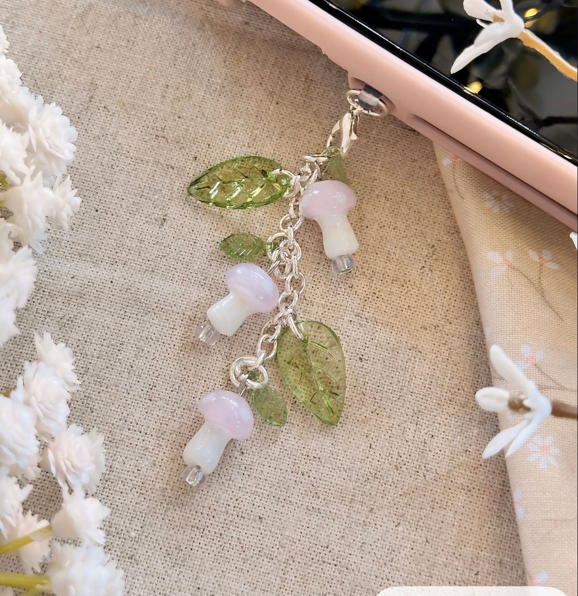Decorative charm with mushrooms and leaves on a textured surface with flowers.