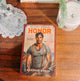 Book titled 'Honor' by Danielle Baker on a wooden surface with decorative items.