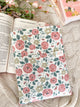 Floral notebook on a textured surface with an open book and flowers.