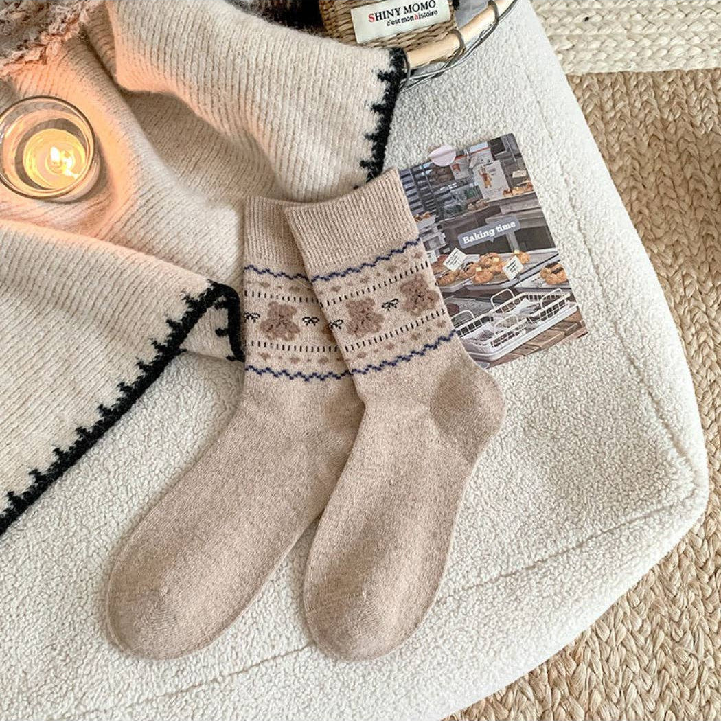 Pair of beige socks with patterned cuffs on a textured surface with a candle and card in the background.