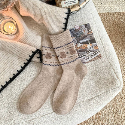 Pair of beige socks with patterned cuffs on a textured surface with a candle and card in the background.